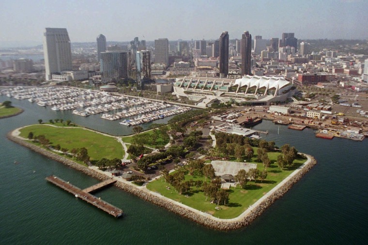 The San Diego Convention Center, with its sail-like roof, is surrounded by the downtown skyline, Embarcadero Park (foreground), the Marriott Marina and San Diego Bay.